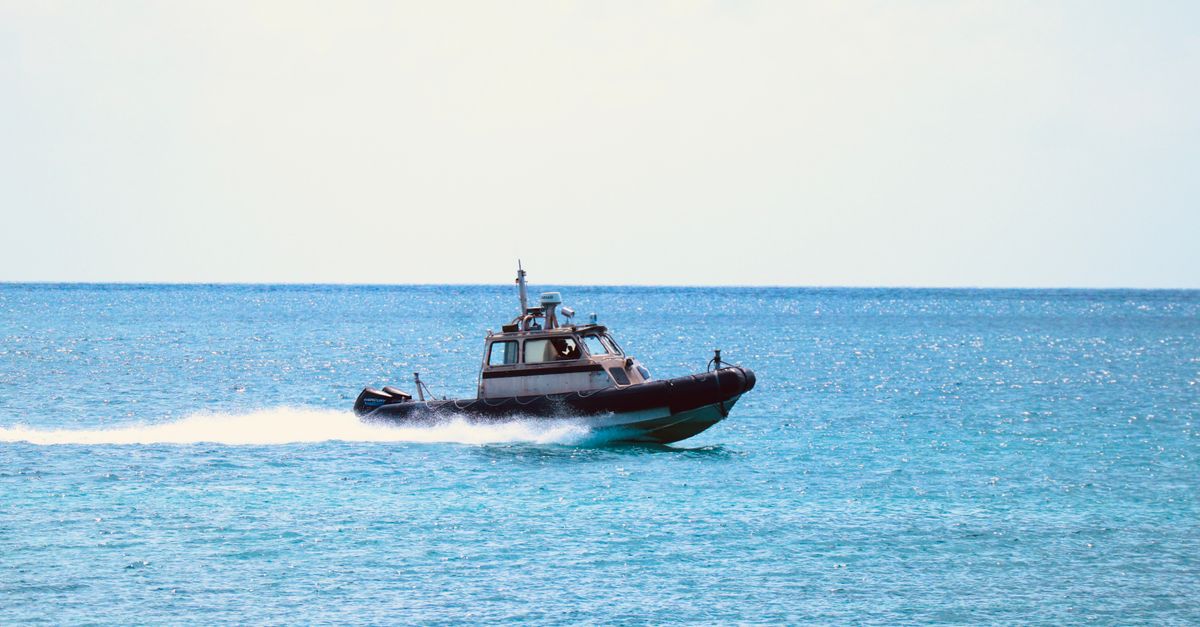 Speedboat at full speed across open water, spray arcing high off the side of the hull