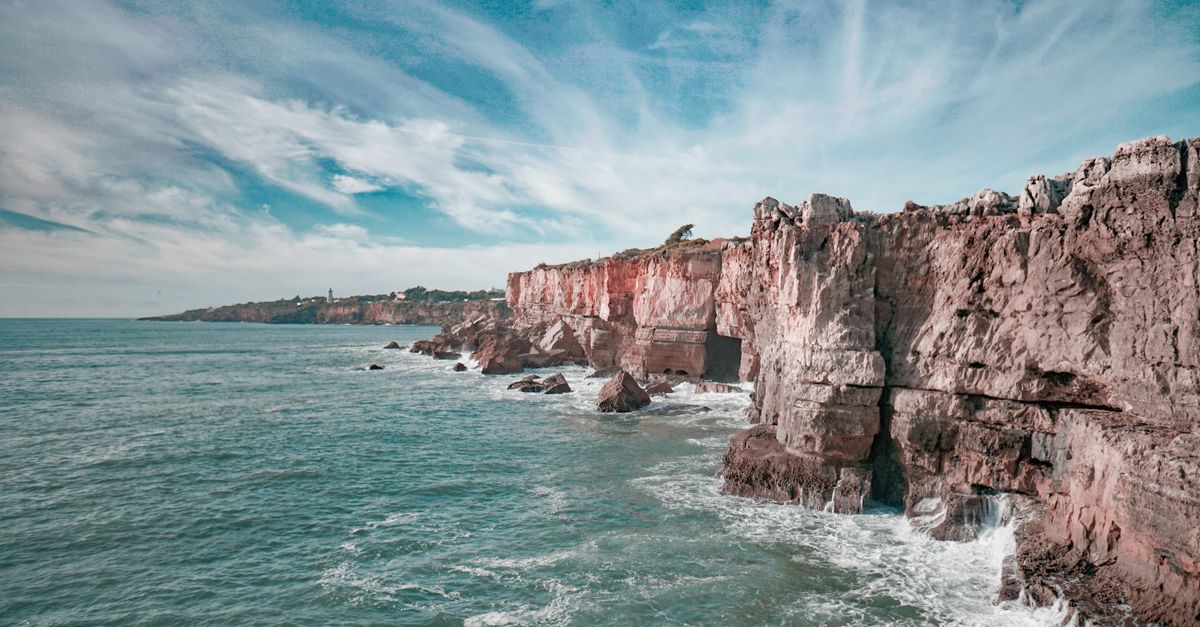 White surf breaking against a jagged rock coastline with open Atlantic behind under a grey sky