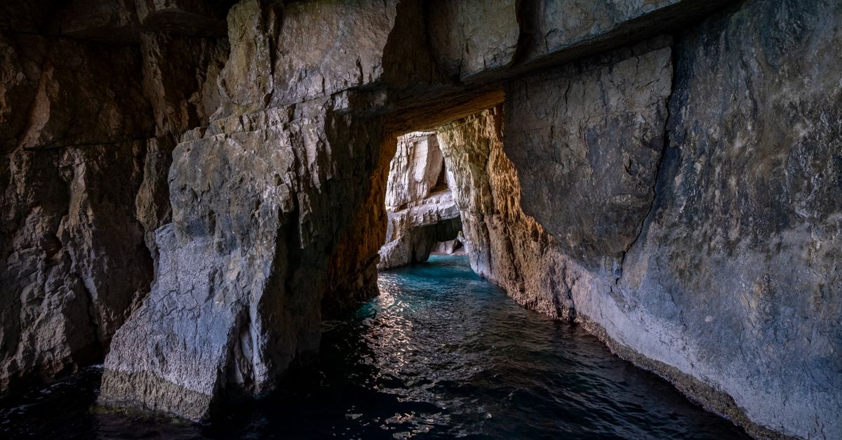 A narrow rock passage opening onto lit turquoise water inside a sea cave