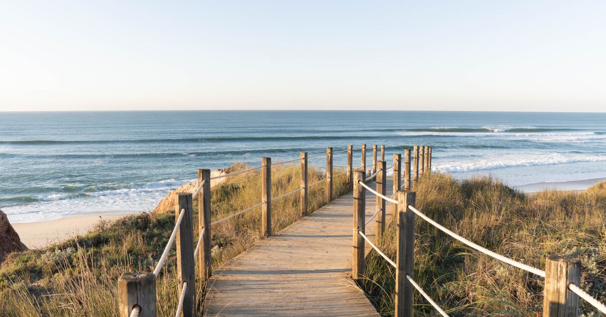 A wooden walkway crosses low dunes towards a wide Atlantic sand beach