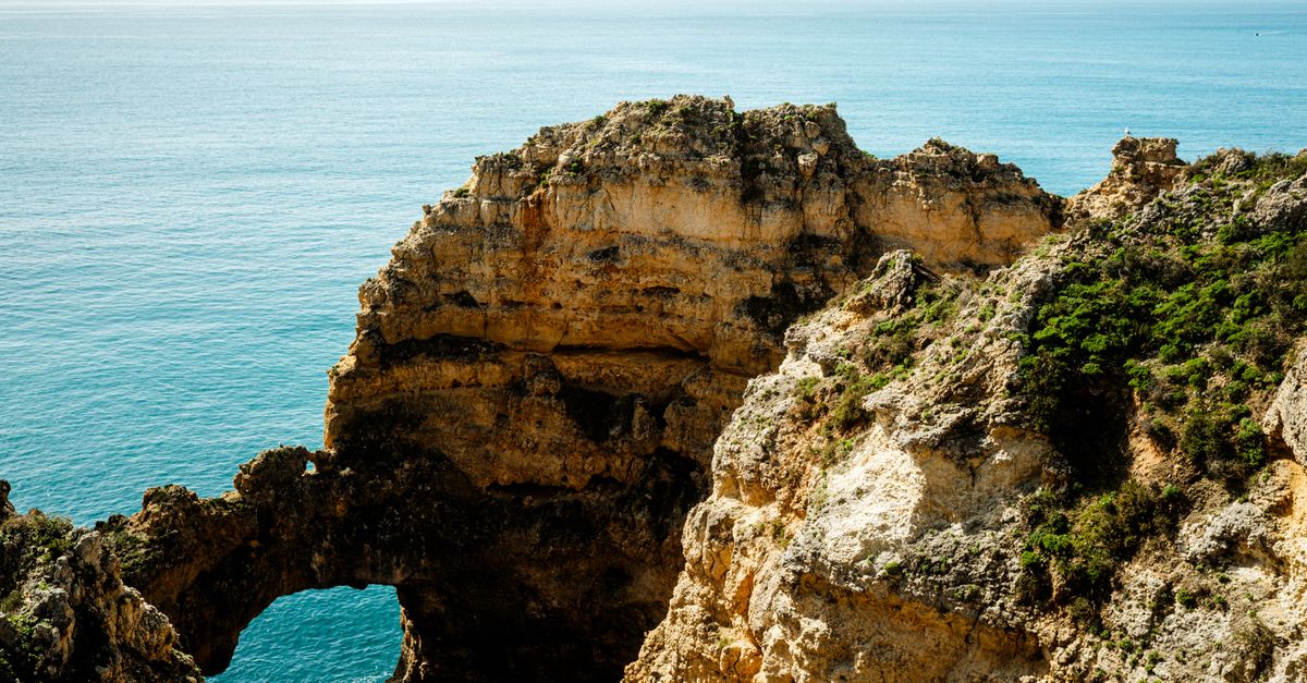A natural arch of ochre sandstone at the tip of the headland, with open Atlantic behind it