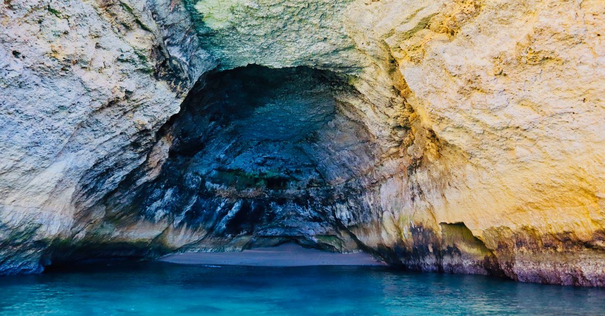 View from inside a sandstone sea cave through the round hole in its roof, sand below and open water beyond